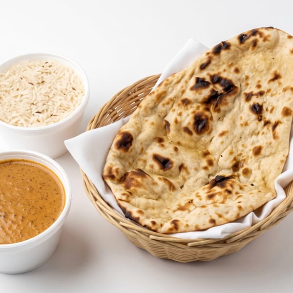A basket of naan bread, a container of rice, and a container of curry sauce.