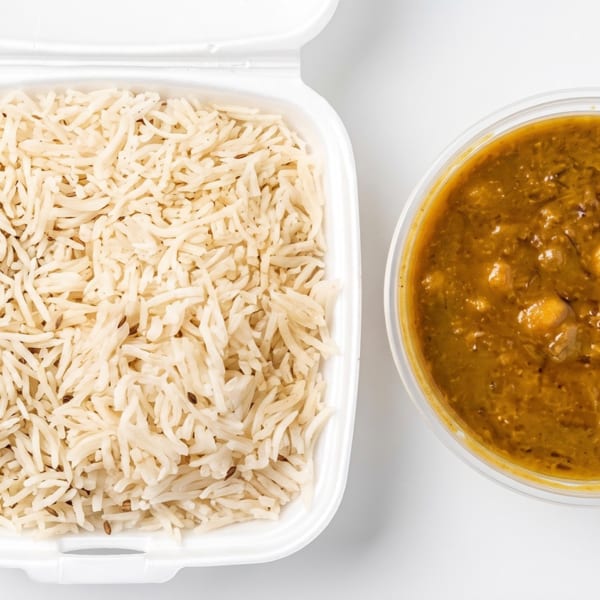 Takeaway containers with cumin rice and a rich, golden lentil curry on a white background.